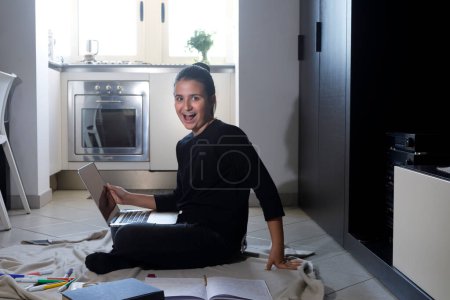 Foto de Chica feliz hace la tarea sentada en el suelo con libros y computadora en su casa - Imagen libre de derechos
