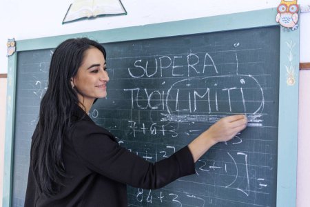 Photo for Dark-haired teacher with green shirt writes on the blackboard the sentence in Italian language "Overcome your limits" - Royalty Free Image