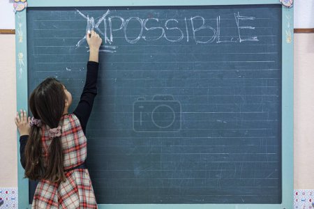 Photo for Female student chalks out the word "impossible" written on a blackboard - Royalty Free Image
