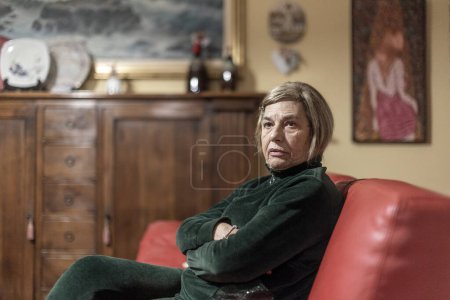 Téléchargez les photos : Triste femme âgée assise dans un fauteuil à la maison - en image libre de droit