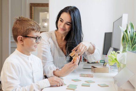 Photo for An educator carries out educational activities with a blond boy sitting in front of a desk in a studio - Royalty Free Image