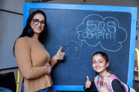 Photo for Teacher and pupil are standing in front of a blackboard with the writing in Italian "s.o.s." assignments - Royalty Free Image