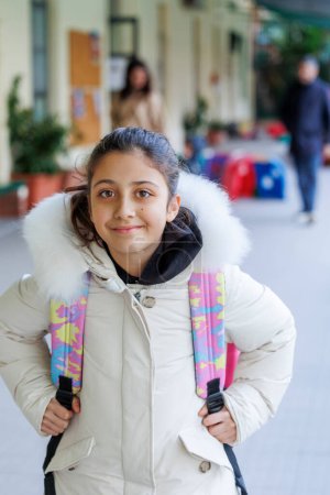 Foto de Retrato de una niña con abrigo y mochila que está a punto de entrar en la escuela - Imagen libre de derechos