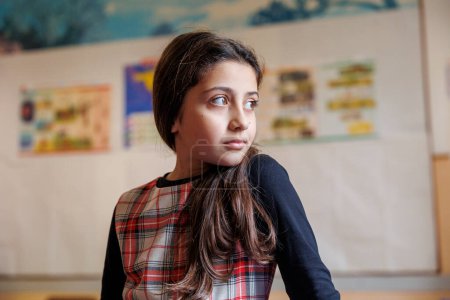 Photo for Pupil dressed in a plaid dress stands with her arms crossed in a classroom of a school - Royalty Free Image