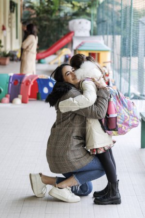 Téléchargez les photos : Une mère emmène sa fille à l'école et la salue avec un câlin chaleureux - en image libre de droit