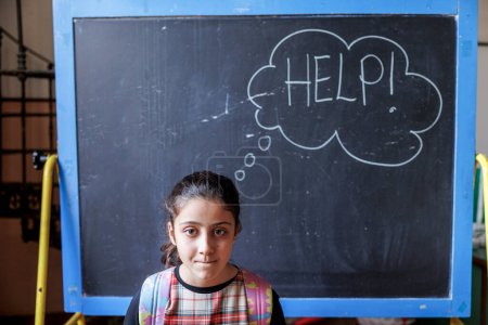 Téléchargez les photos : Petite fille devant un tableau noir qui dit "Aide-moi" - en image libre de droit