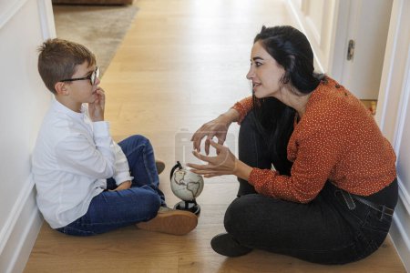 Photo for Adult girl with dark hair shows a little boy a globe while they are sitting on the floor at home - Royalty Free Image