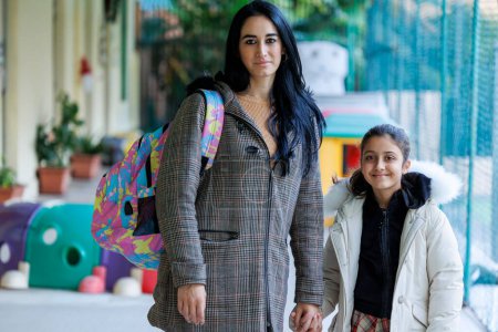 Foto de Una madre acompaña a su hija a la escuela y le da recomendaciones antes de entrar, ajustando su chaqueta - Imagen libre de derechos