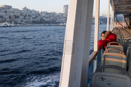 Téléchargez les photos : Fille en veste rouge regarde dans la distance tout en traversant avec un ferry - en image libre de droit