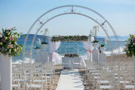 Téléchargez les photos : Arche de mariage décorée de belles fleurs sur la plage - en image libre de droit