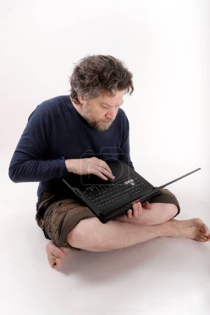 Mann sitzt auf dem Boden und arbeitet an seinem Laptop