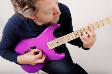 anonymous man practicing guitar sitting down white background