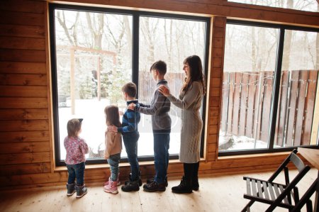 Téléchargez les photos : Mère et quatre enfants dans une maison en bois moderne contre une grande fenêtre. - en image libre de droit