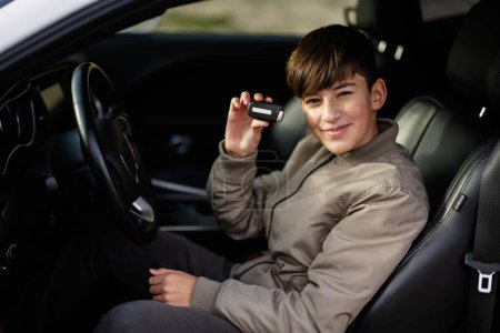 El chico adolescente se sienta en el coche del músculo. Joven adolescente conductor mostrando llaves.