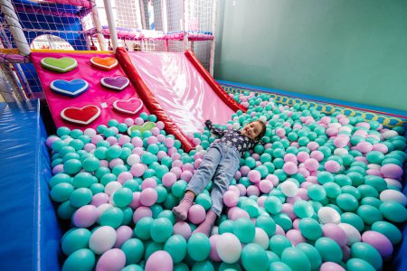 Photo for Happy girl playing at indoor play center playground. Lying at color balls in ball pool. - Royalty Free Image