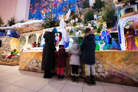 Foto de Mother with three children visit Christmas nativity crib scene in church. - Imagen libre de derechos