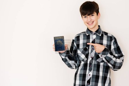 Téléchargez les photos : Young teenager boy holding Bhutan passport looking positive and happy standing and smiling with a confident smile against white background. - en image libre de droit