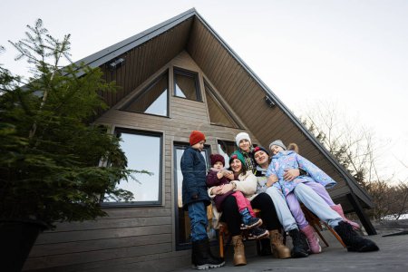 Téléchargez les photos : Grande famille avec quatre enfants assis sur la terrasse hors réseau petite maison dans les montagnes. - en image libre de droit