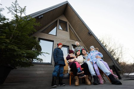 Téléchargez les photos : Grande famille avec quatre enfants assis sur la terrasse hors réseau petite maison dans les montagnes. - en image libre de droit