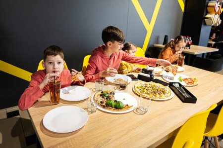 Téléchargez les photos : Quatre enfants mangeant de la pizza italienne en pizzeria. Les enfants mangent au café. Garçon boire du jus. - en image libre de droit