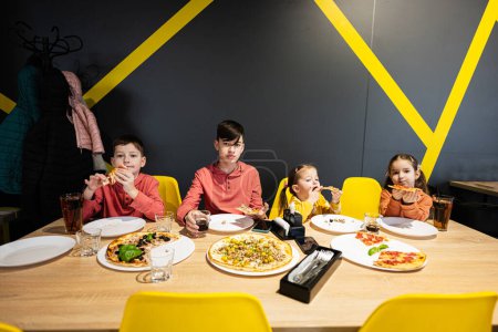 Téléchargez les photos : Quatre enfants mangeant de la pizza italienne en pizzeria. Les enfants mangent au café. - en image libre de droit