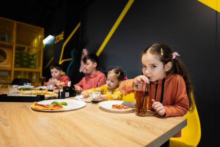 Téléchargez les photos : Quatre enfants mangeant de la pizza italienne en pizzeria. Les enfants mangent au café. Fille boire du jus. - en image libre de droit