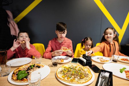 Téléchargez les photos : Quatre enfants mangeant de la pizza italienne en pizzeria. Les enfants mangent au café. - en image libre de droit