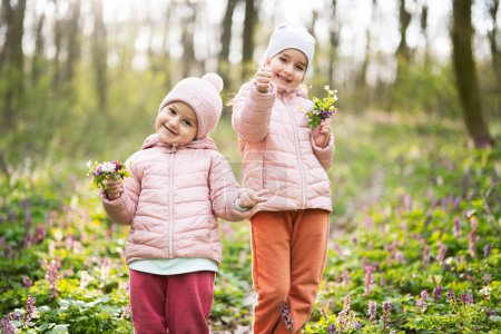 Téléchargez les photos : Portrait de deux petites sœurs avec bouquet de fleurs sur une forêt ensoleillée. Plein air printemps loisirs concept. - en image libre de droit