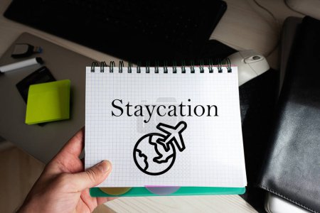 Staycation Wort auf Notizbuch hält Mann gegen Desktop.