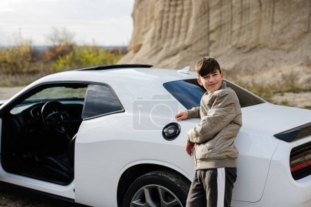 Téléchargez les photos : Adolescent garçon stand près de blanc muscle car. Jeune adolescent conducteur. - en image libre de droit