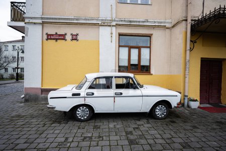 Photo for Lutsk, Ukraine - March, 2024: A classic white soviet Moskvitch sedan car carefully parked by a colorful building facade with traditional European architectural elements and cobblestone pavement. - Royalty Free Image