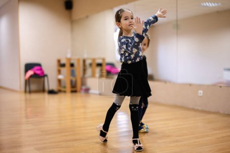 A young girl in a dance studio practicing her dance moves in front of a mirror, showcasing focus and grace.