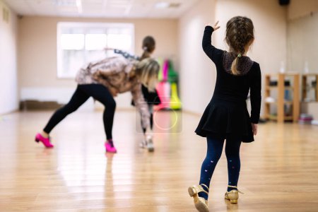 A young girl in a dance class practicing with guidance from an instructor. She is wearing a black outfit and following dance steps.