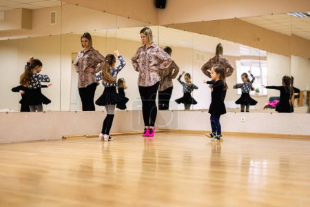 A dance instructor guiding young girls in a ballet studio with mirrored walls, focusing on technique and form.