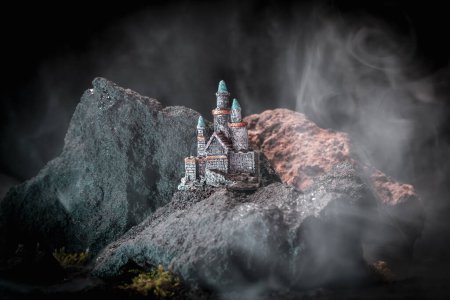 Foto de El castillo medieval está rodeado de rocas, montañas, y el humo está ondeando a su alrededor, como los efectos de la niebla o el fuego. Una gran cantidad de colores. Magia e intriga reinan en ella. Musgo verde. - Imagen libre de derechos