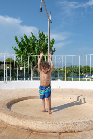 Kind genießt an einem sonnigen Tag eine Dusche am Pool.