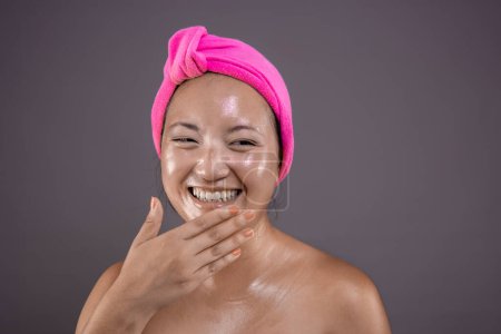 Mujer asiática sonriendo con toalla de cabeza rosa