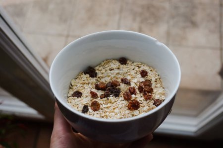 Téléchargez les photos : Un bol blanc de muesli composé de flocons d'avoine bio et de pamplemousses séchées, un exemple de repas léger et sain pour le petit déjeuner du matin - en image libre de droit