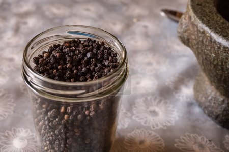 Téléchargez les photos : Pot en verre plein de grains entiers de poivre noir cru, un condiment épicé de l'Inde, bien connu et largement utilisé dans la cuisine orientale exotique pour améliorer le goût des plats - en image libre de droit