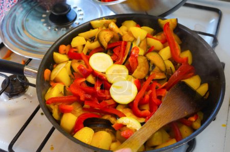 Foto de Homemade cooking of mixed fried vegetables comprising red peppers, potatoes, courgettes and carrots in a stovepan - Imagen libre de derechos