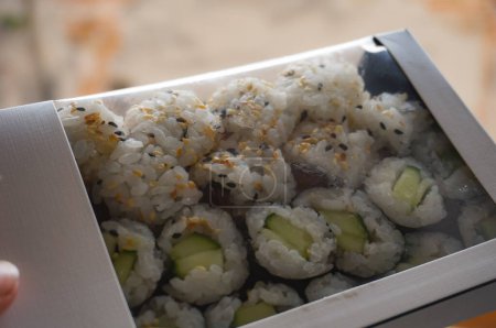 Téléchargez les photos : A box of artisanal Japanese sushis based on rice and fish to takeaway, ordered in an Asian restaurant in Toulouse, France ; the sushis are stuffed with avocado or salmon and feature sesame seeds - en image libre de droit