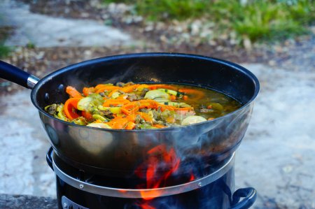 Mixed fried vegetables (peppers, zucchini, mushrooms, broccoli with some meat) cooked in the Asian fashion in a skillet above a wood stove burner, from which an orange flame emanates