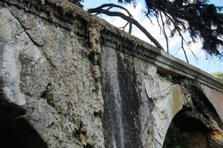 Foto de Restos de un antiguo acueducto en ruinas, en un parque arbolado en Beaujolais, Francia, parcialmente derrumbado, dañado por la humedad y cubierto por hongos y salitre, con agua goteando sobre la piedra - Imagen libre de derechos