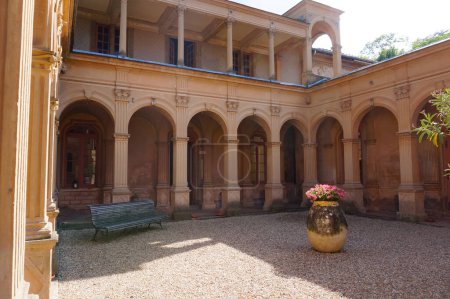 Photo for Near Lyon, France - June 2019 - The magnificent gallery of arcades of the Italian cloister of Saint Trys Castle, built in an oriental exotic style around a small gravel courtyard with a wooden bench - Royalty Free Image