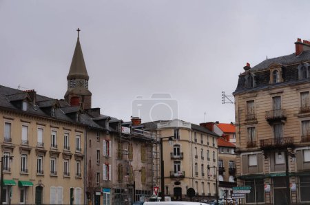 Photo for Aurillac, France - Feb. 2022 - Townhouses on Pierre Semard Square, in front of the railway station, with the tower of Sacre-Coeur Church in the background ; Aurillac is the chief-town of the Cantal - Royalty Free Image