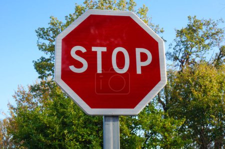 Foto de Señalización vial roja y blanca con superficie reflectante, en Francia: una señal de stop, en forma de octágono sobre un poste metálico, con árboles en una atmósfera soleada en el fondo - Imagen libre de derechos