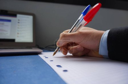Téléchargez les photos : La main d'un homme sur un bureau, au-dessus d'une feuille de papier, tient des stylos à bille - en image libre de droit