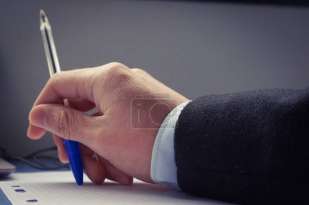 Photo for A man's hand on a desk, above a sheet of paper, holds a blue ballpoint pen - Royalty Free Image