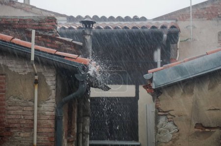 Téléchargez les photos : Gouttières débordantes d'eau qui fuient des toits de tuiles d'une vieille maison en briques délabrée à Toulouse, dans le sud de la France, par une journée pluvieuse et brumeuse avec un impressionnant nuage éclaté et des vents forts - en image libre de droit