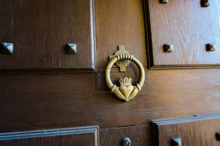 Téléchargez les photos : Frappeur de porte en vieux métal, sculpté selon la représentation traditionnelle d'un anneau irlandais Claddagh : deux mains serrées (symbole de l'amitié) tenant un cœur (amour) surmonté d'une couronne (loyauté) - en image libre de droit